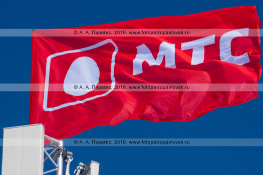 Фотографии флага c логотипом МТС, развевающегося на ветру в солнечную погоду на фоне ясного синего неба