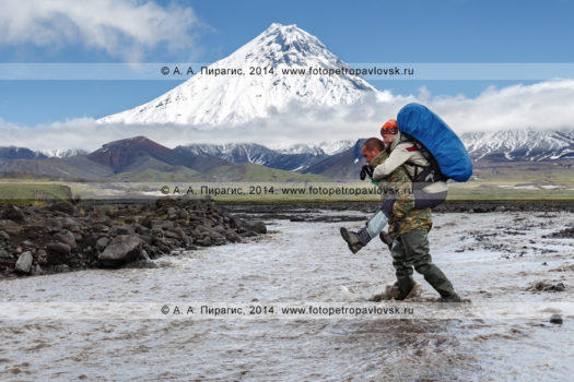 Фотография: пеший туризм на Камчатке — гид переносит девушку-туристку (с рюкзаком за плечами) через горную реку Студеную